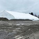 a giant white tent sits in the middle of a muddy work area. a construction truck is on one side and is small in comparison